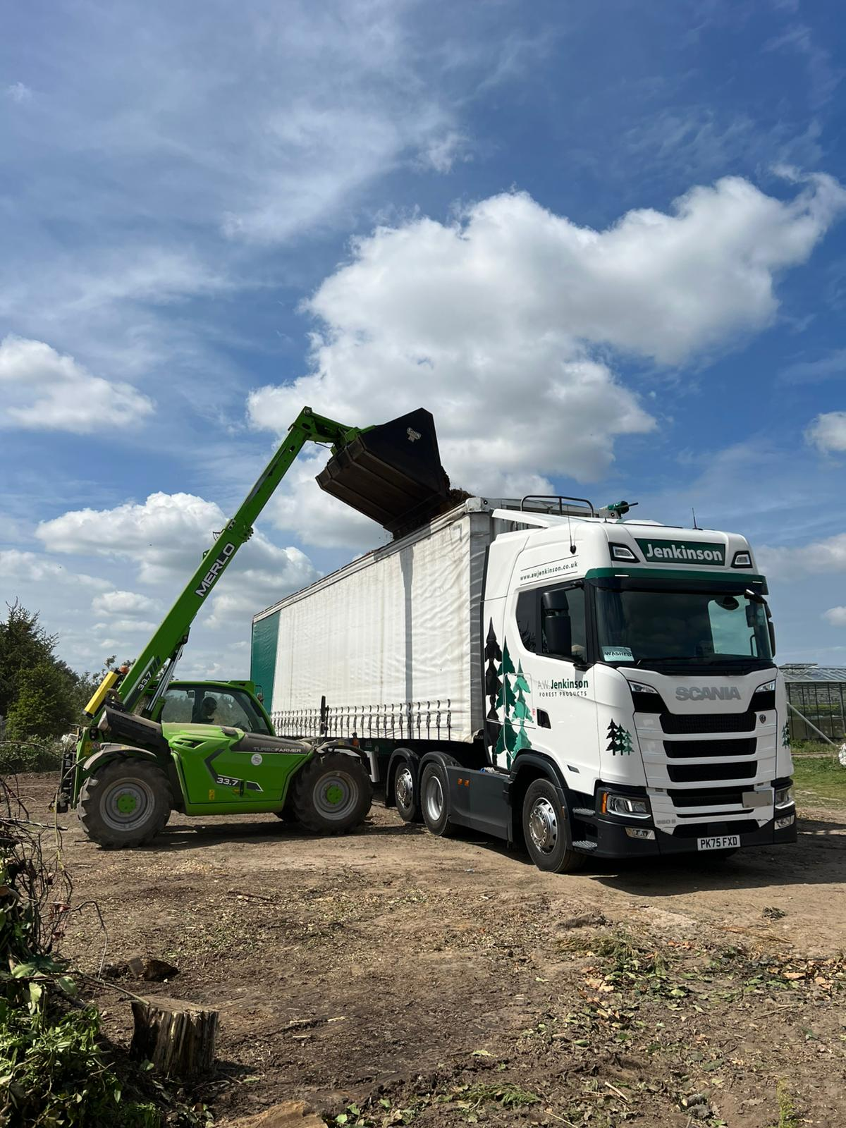 Telehandler loading recycled biomass waste into an A.W. Jenkinson lorry for renewable energy processing.